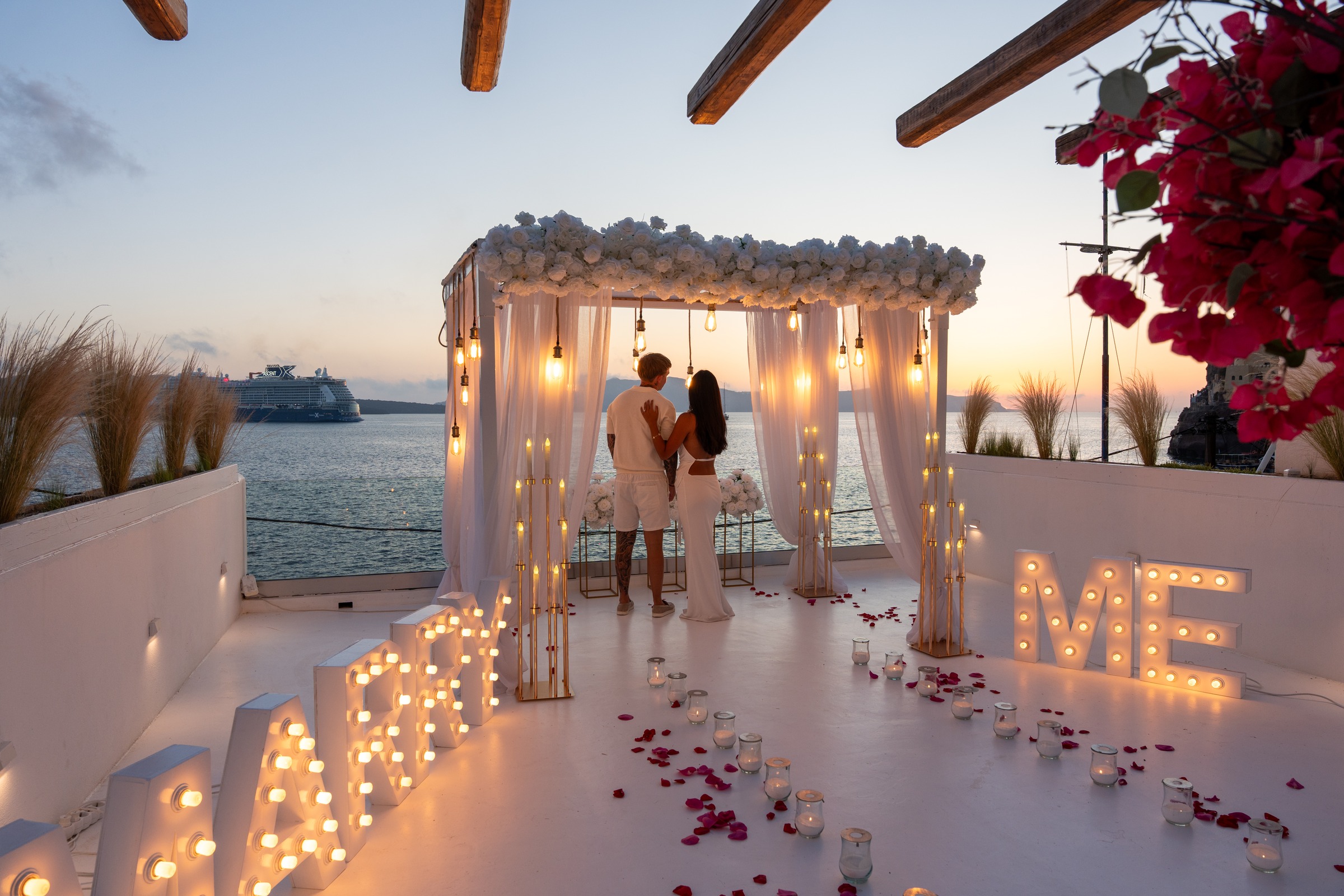 Marry Me written in marquee lights at a dusk proposal terrace in Santorini